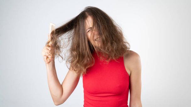 Une femme grimace quand ça fait mal, un peignage complexe de cheveux indisciplinés emmêlés avec un peigne. Photo de haute qualité - Photo, image