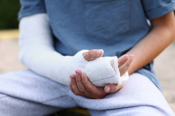 a child's arm is broken. little boy with a fractured limb outdoors. fracture injury in the summer holiday. kid is moving fingers in plaster cast on the arm - 写真・画像