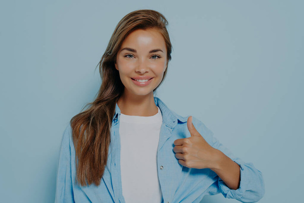青い長袖のシャツを着た幸せな若い白人女性が親指を立てて笑顔で、誰かへのサポートと尊敬を示しています。ボディランゲージ。それは好きよ。いい仕事だ - 写真・画像