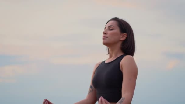 Молодая здоровая красивая женщина в спортивной одежде практикует йогу на природе. Девушка сидит в позе лотоса на траве и медитирует с закрытыми глазами, концепция медитации памятования - Кадры, видео
