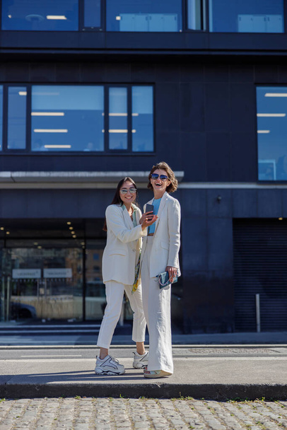 Οι γυναίκες με μοντέρνα ρούχα γελάνε και περπατάνε έξω κοντά στο επιχειρηματικό κέντρο - Φωτογραφία, εικόνα