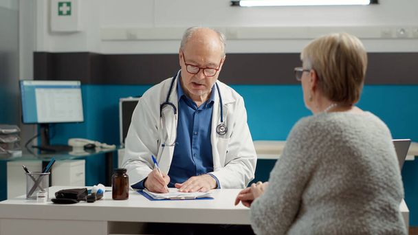 Male doctor using recovery medication to give prescription paper to retired patient in medical office. Writing information to give treatment for illness diagnosis, health care system. - Foto, imagen