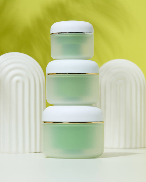 Groene pot voor cosmetica op een witte tafel. Verpakking voor room, gel, serum, reclame en productpromotie - Foto, afbeelding