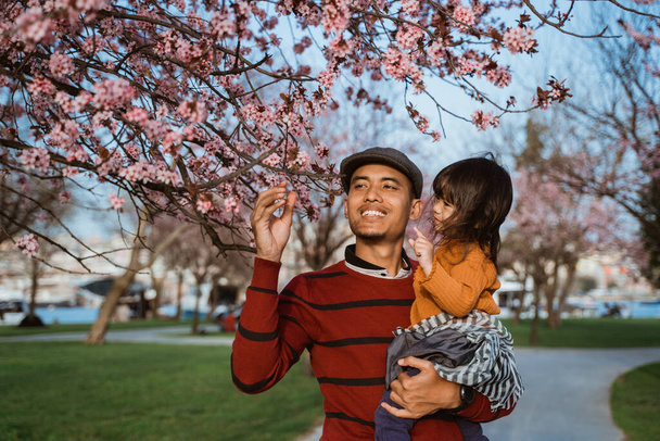 happy father and daughter looking at cherry blossom in the park - Photo, image