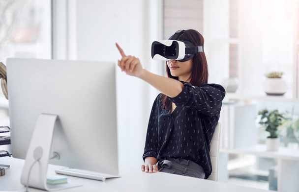 Her business knows no bounds. a young businesswoman wearing a VR headset while working in her office - Foto, Bild