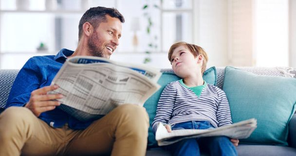Переконатися, що він знає, що знання це сила. красивий батько і син читають газету разом, сидячи на дивані вдома
 - Фото, зображення