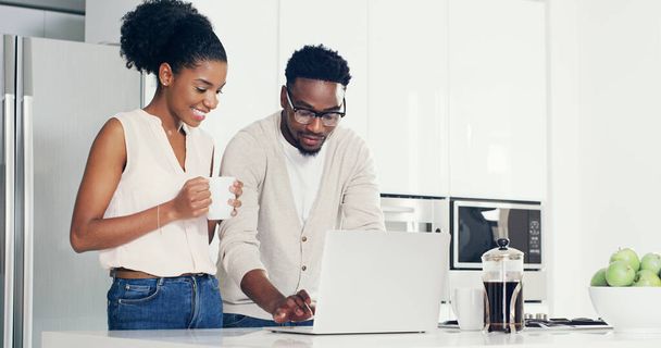 Hes always got interesting videos to show me online. a cheerful young couple using a laptop together in the kitchen at home - 写真・画像