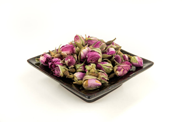 Dehydrated pink rose buds in a black ceramic plate - Valokuva, kuva