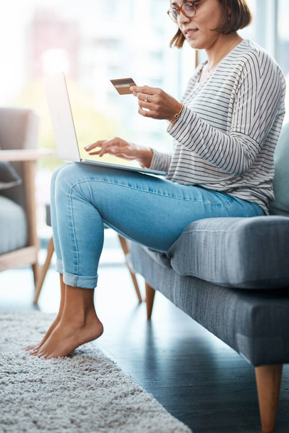 Let me order this before it gets sold out. a young woman using her laptop and credit card on the sofa at home - Foto, afbeelding