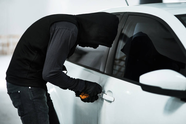 No car is safe from his wrath. a masked criminal picking the lock of a car door inside a parking lot - Photo, Image