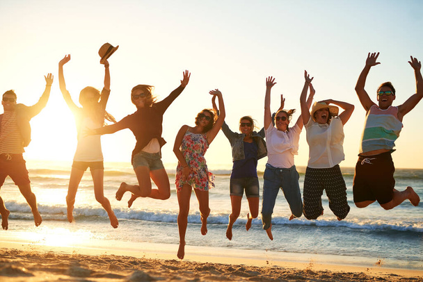 The sweet joys of summer... Full length shot of a group of young friends jumping into the air at the beach - Photo, Image