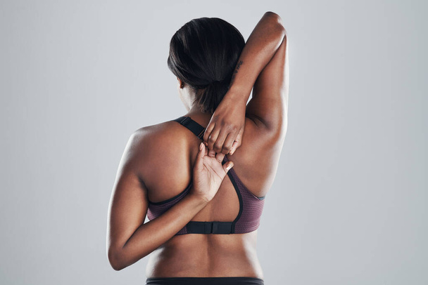Nothing is a stretch too far. Rearview shot of an athletic young woman stretching her arms against a grey background - Foto, Bild