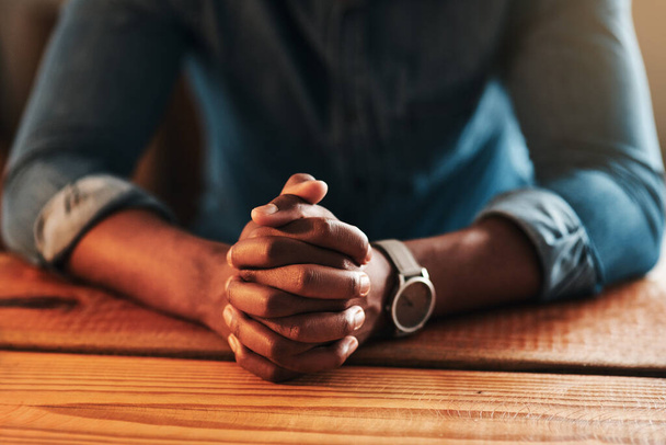 Quiet, calm and spiritual man praying while sitting with his hands folded alone at home. Close up praying, hopeful and religious, Christian male saying a daily prayer in the morning at a table. - Zdjęcie, obraz