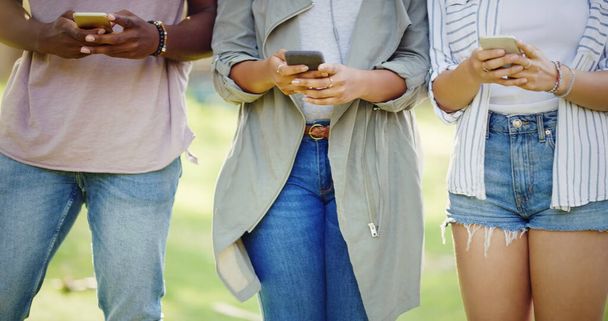 Συζητήσεις νέας εποχής. μια αγνώριστη ομάδα φίλων που ο καθένας χρησιμοποιεί τα κινητά του ενώ στέκεται σε ένα πάρκο στην ύπαιθρο - Φωτογραφία, εικόνα