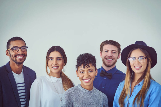We shine when we work as a team. Studio portrait of a group of young businesspeople smiling while standing against a grey background - Zdjęcie, obraz