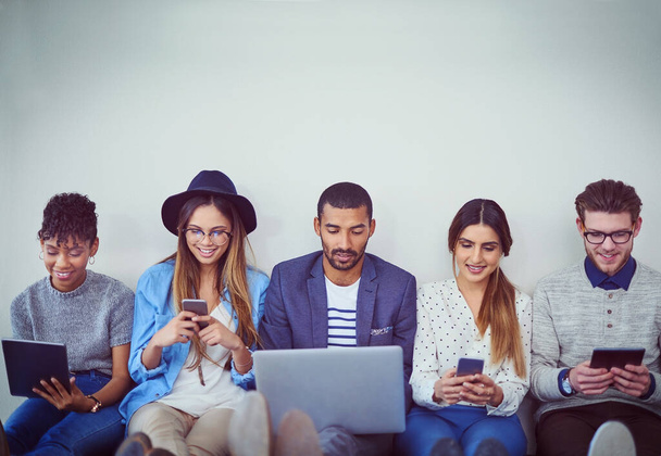 Making smart business choices using smart connections. Studio shot of a group of young businesspeople using wireless technology while sitting in line against a grey background - Foto, afbeelding