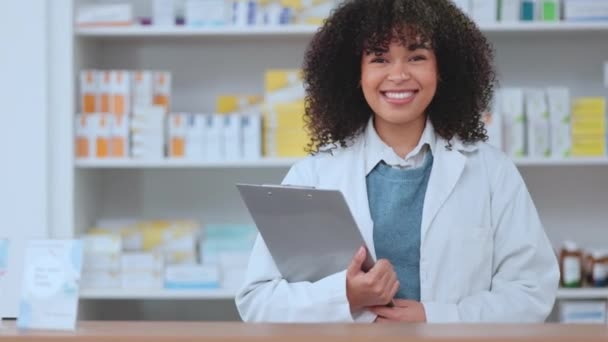 Portrait of happy pharmacist holding a clipboard while working in a modern drug store. Smiling health care worker checking stock, doing inventory and making a list of supplies, ready to assist. - Video