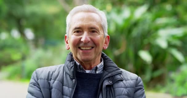 Healthy, smiling face of a senior man enjoying his retirement outdoors in a green park or garden. Happy and cheerful portrait of a single pensioner with bright expression and copy space background. - Imágenes, Vídeo