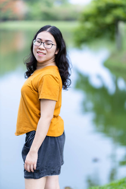 a portrait of beautiful happy asian woman traveler wearing yellow orange dress stylish hipster lifestyle on the street outdoors at summer day in park or in background - Photo, Image