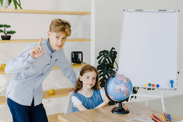 Teenage girl and boy siting near table with globe in classroom. Teen schoolboy and schoolgirl doing project together at school - Foto, imagen