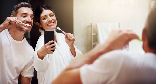 Look at our superstar smiles. a mature couple taking selfies while brushing their teeth in the bathroom at home - Fotoğraf, Görsel