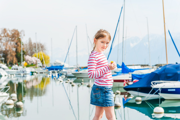 Cute little girl resting next to lake, weraing red and white top and jeans skirt - Photo, Image