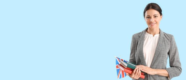 Female English teacher with books and UK flag on light blue background with space for text - 写真・画像