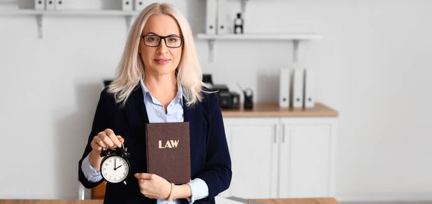 Зріла жінка-суддя з будильником і юридичною книгою в офісі
 - Фото, зображення