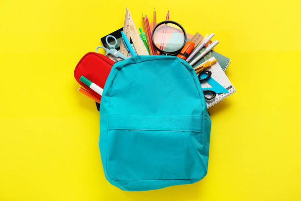 School backpack with stationery supplies on yellow background - Foto, Imagen
