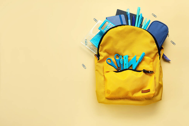 Yellow backpack with school stationery on beige background - Photo, Image