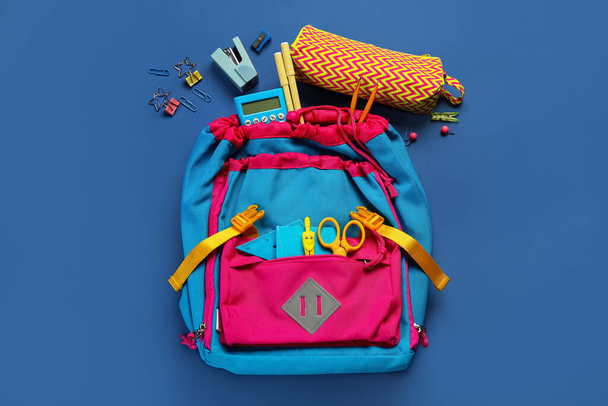 School backpack with stationery on blue background - Fotó, kép