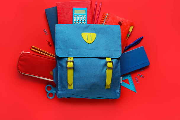 Blue backpack with school stationery on red background - Foto, afbeelding
