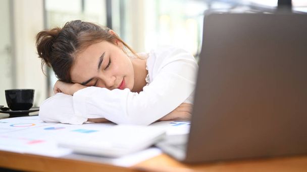 Tired female office worker having a nap at her desk with her head lying on her arm, tired from work. - Foto, Imagen