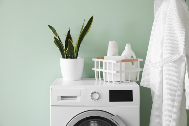 Basket with detergent and houseplant on washing machine near green wall - Fotoğraf, Görsel