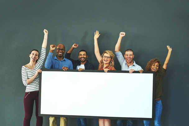 Happy, diverse and cheering marketing team with a blank card, poster or billboard with copyspace in studio on a grey background. A group of smiling business people celebrating and endorsing a product. - Foto, Bild