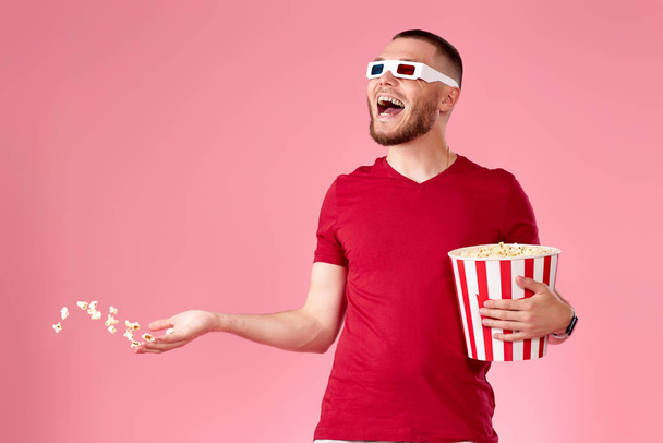 young man in 3d glasses throwing up and eating popcorn on pink background - Photo, Image