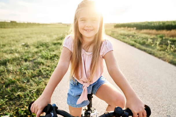 Portrait of little caucasian girl sitting on bike at sunset time - 写真・画像
