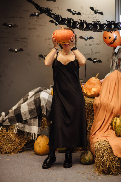Young sexy fun gothic girl celebrating Halloween. A man holds a pumpkin head as his head. Halloween season mood. - Foto, Imagem