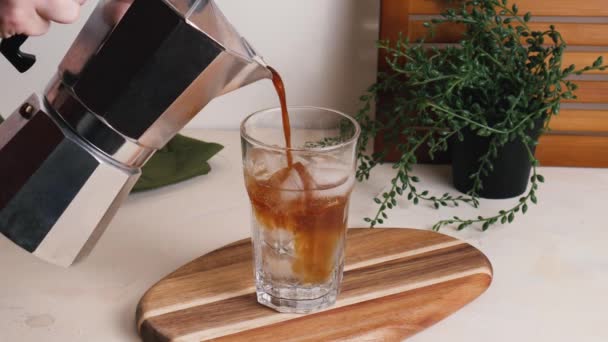 Nalít espresso z hrnce moka do sklenice s tonikem a kostkami ledu. Šumivé letní nápoj na dřevěné desce - Záběry, video