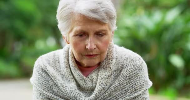 Sad, upset and frustrated senior woman alone outdoors in a nature park during spring closeup. Portrait of a depressed, unhappy and worried elderly female with grey hair sitting and feeling lonely. - Imágenes, Vídeo