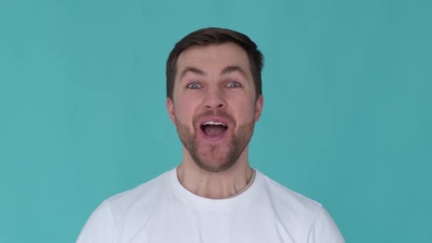 Handsome guy with a wow expression. Close up of young man posing on blue background. Portrait of a smiling european man who raises his thumbs up - Filmagem, Vídeo
