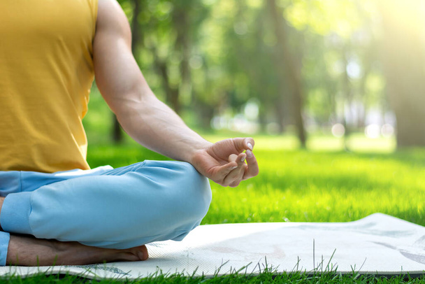 Un jeune homme pratique le yoga dans le parc. Yoga asanas dans le parc de la ville, journée ensoleillée. Concept de méditation, bien-être et mode de vie sain - Photo, image