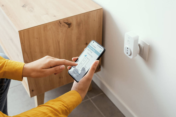 Woman setting a smart plug at home using her smartphone, smart home and domotics concept - Foto, imagen