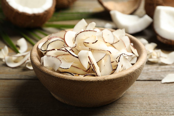 Tasty coconut chips in bowl on wooden table - Φωτογραφία, εικόνα