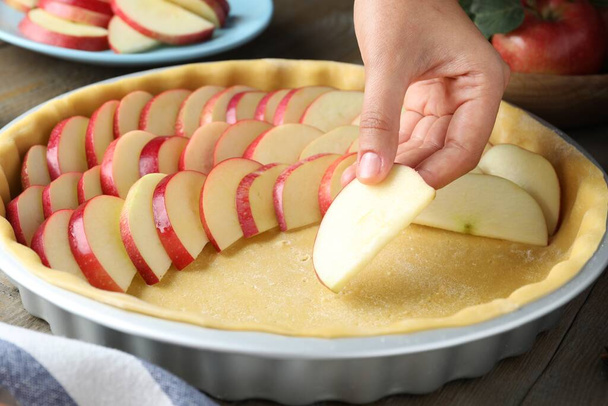 Woman putting apple slices into dish with raw dough at wooden table, closeup. Baking pie - Фото, зображення