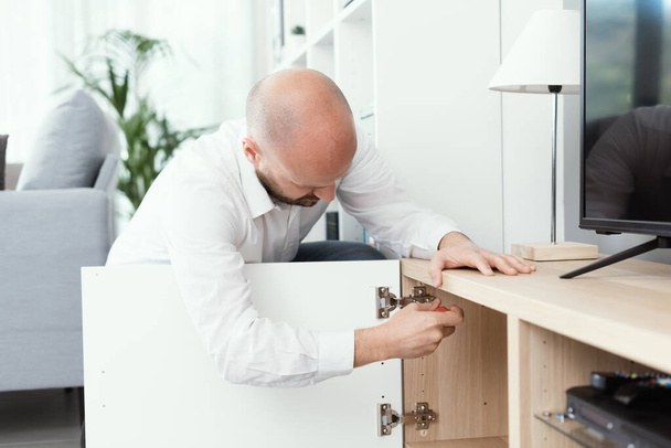Man repairing a loose cabinet door hinge at home using a screwdriver - Photo, image