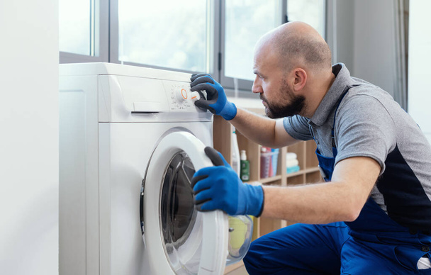 Professional technician checking a washing machine, he is adjusting a knob, home repair concept - Fotoğraf, Görsel