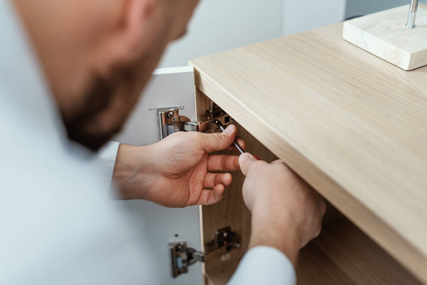 Man repairing a loose cabinet door hinge at home using a screwdriver - 写真・画像