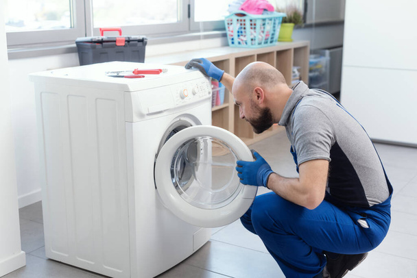Professional technician checking a washing machine, he is adjusting a knob, home repair concept - Foto, Imagem