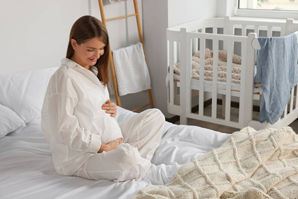 Happy young pregnant woman in pajamas on bed at home - Photo, Image